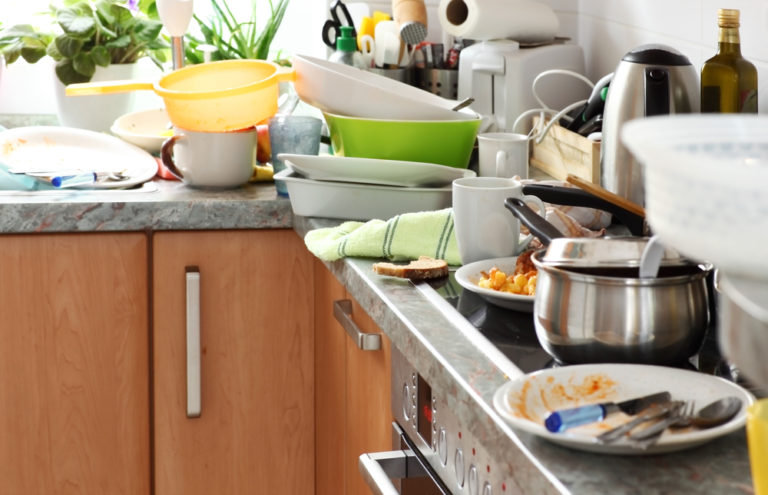 Messy and cluttered kitchen with pots and pans and dirty dishes stacked on the granite countertop and range. Clutter can be a serious safety issue, particularly for older adults.